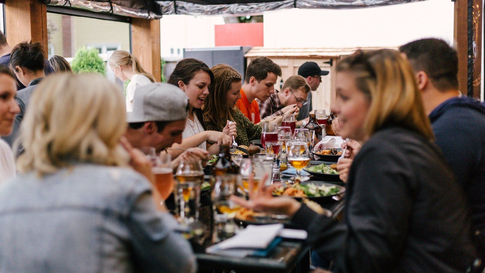 A warm dinner table filled with food dishes and glassware where friends gather in evening light.