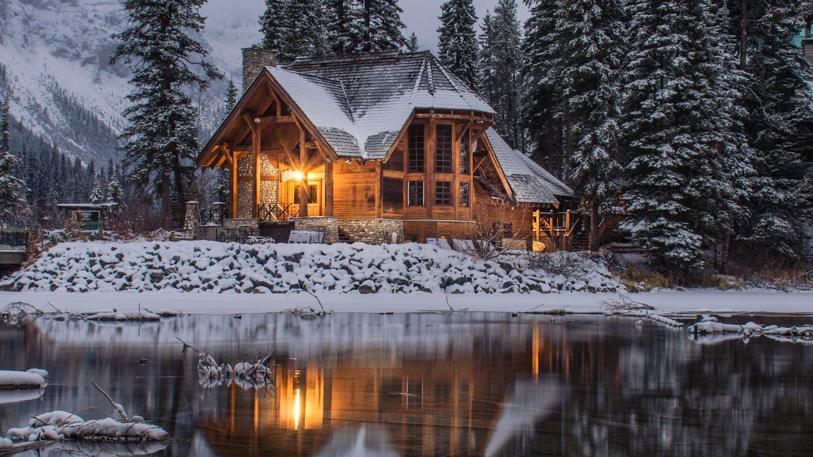 A rustic wooden cabin table with an open journal beside a window overlooking pine trees.