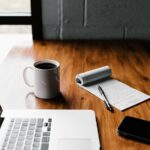 A clean home office desk with a notebook, coffee mug, and organized financial planning sheets.