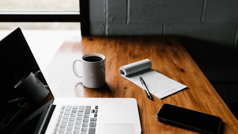 A clean home office desk with a notebook, coffee mug, and organized financial planning sheets.